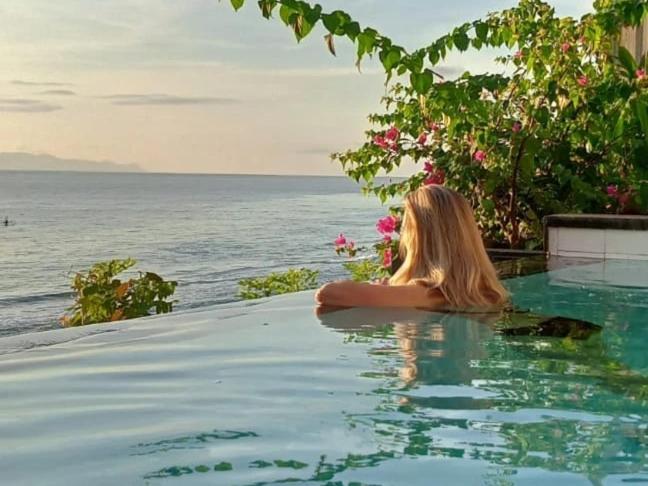 a woman sitting in a swimming pool looking at the ocean at The Sagara Penida Nusa Penida in Nusa Penida