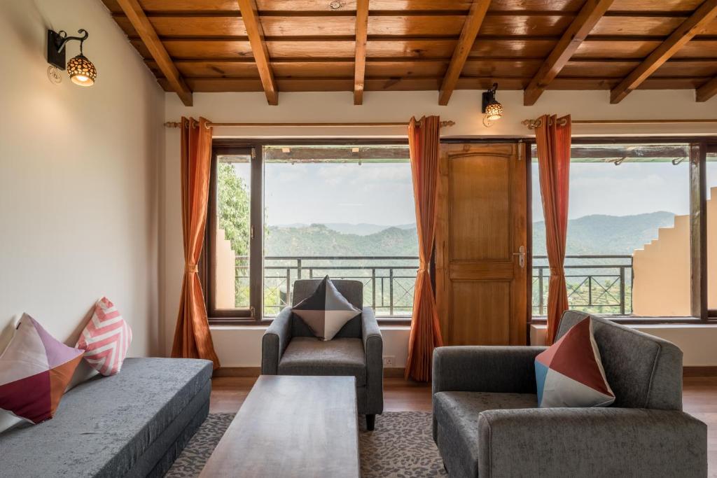 uma sala de estar com um sofá, cadeiras e janelas em Belle Vue, Studio overlooking the hills w wifi by Roamhome em Mukteshwar