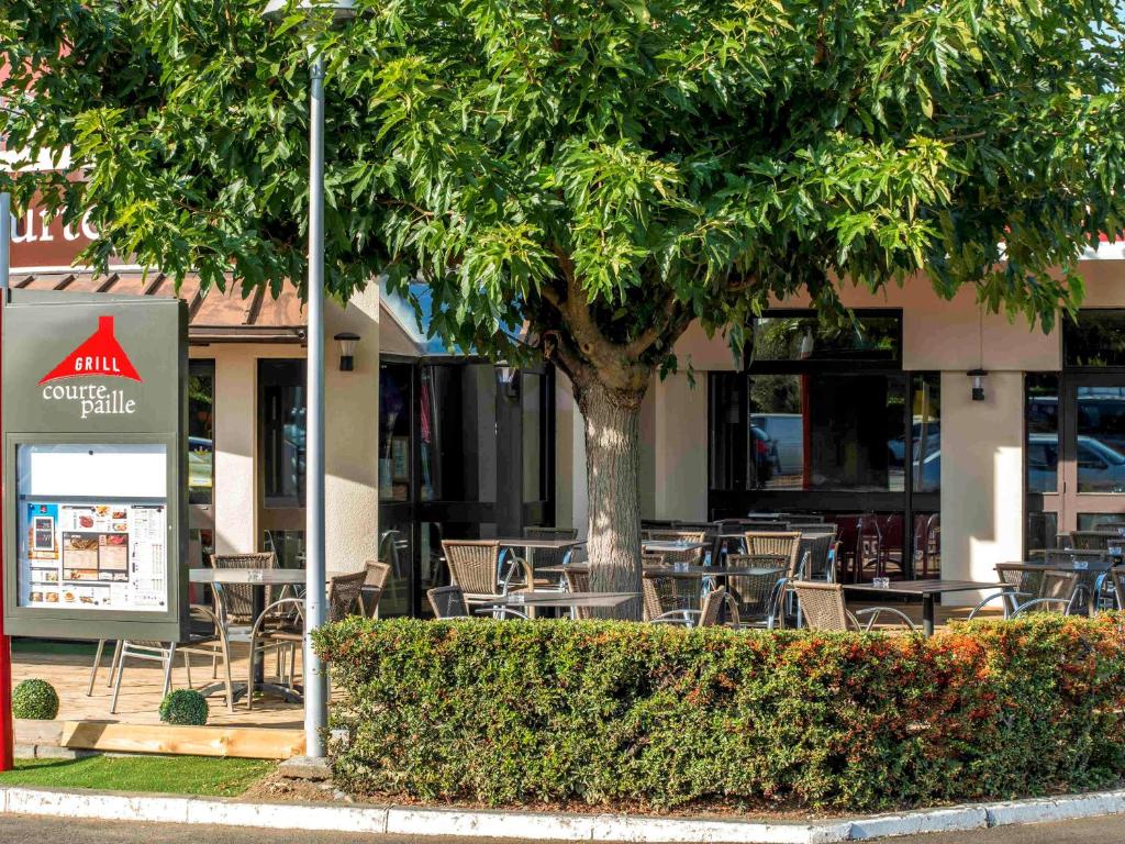 una cafetería al aire libre con mesas, sillas y un árbol en ibis Toulouse Aeroport en Blagnac