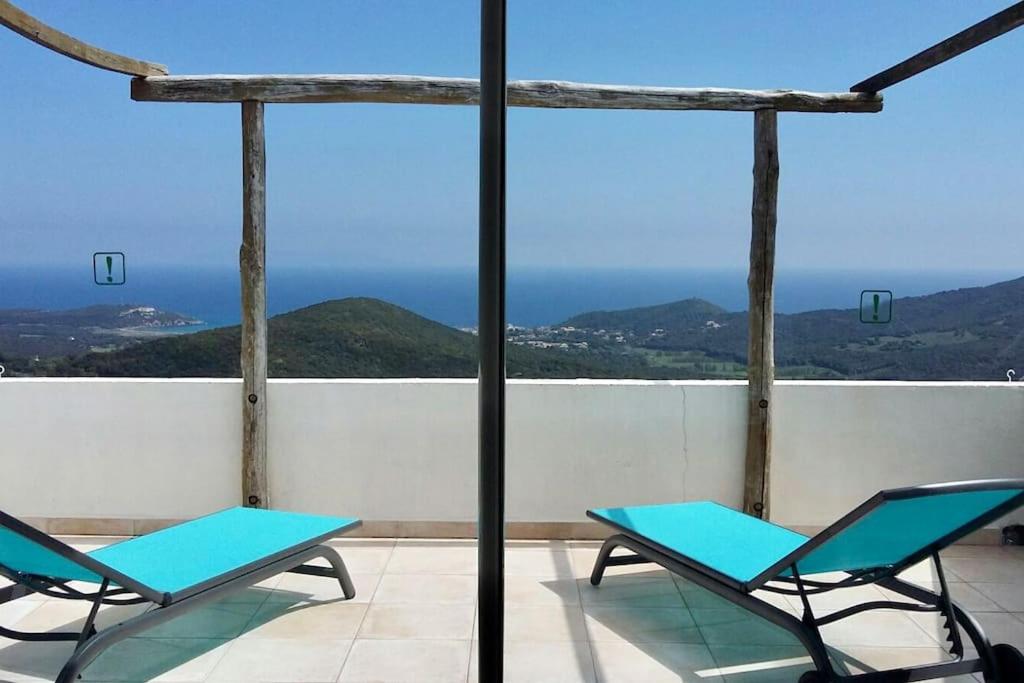 Rogliano Maison de charme avec vue panoramique في Rogliano: كرسيان زرقان على شرفة مطلة على المحيط