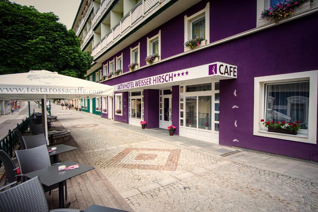 un bâtiment violet avec des tables et un parasol dans une rue dans l'établissement AKTIVHOTEL Weisser Hirsch, à Mariazell