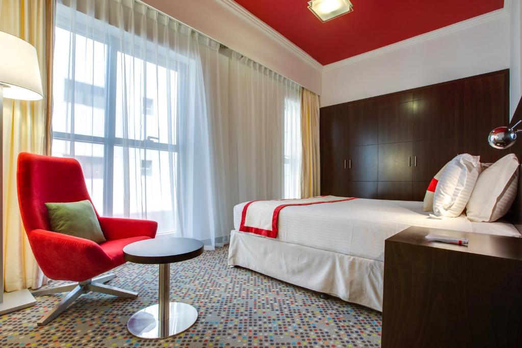 um quarto de hotel com uma cama e uma cadeira vermelha em MENA ApartHotel Albarsha At The Mall em Dubai