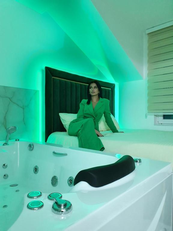 a woman sitting on a bed in a green room at Apartmani Parice in Novi Pazar