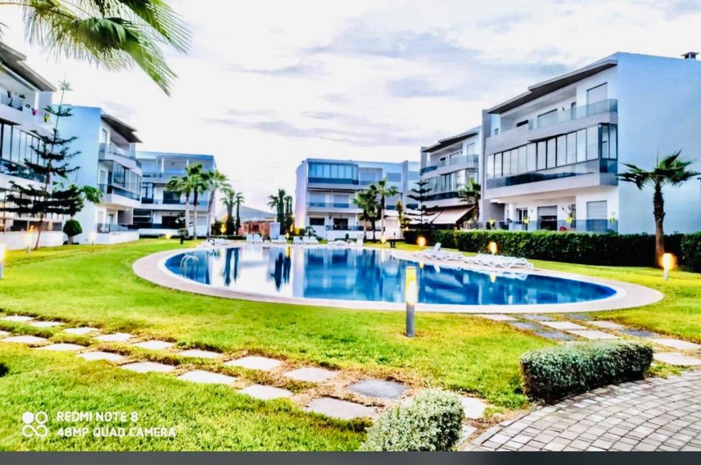 uma imagem de uma piscina em frente a alguns edifícios de apartamentos em Appartement Blanca Beach em Sidi Rahal