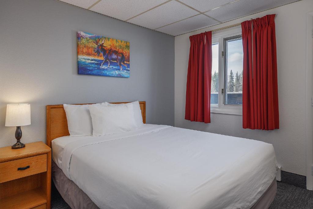 Golden North Inn في فيربانكس: غرفة نوم بسرير ابيض كبير مع ستائر حمراء