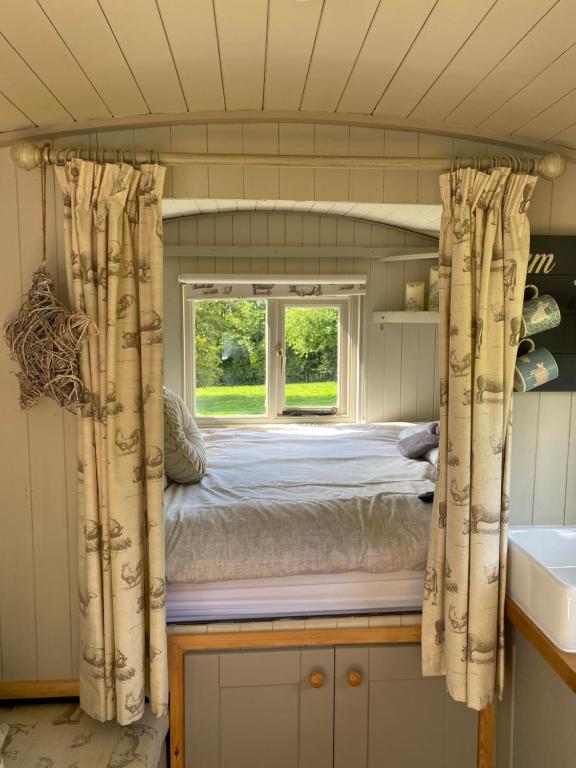 a bed in a small room with a window at The Orchard Shepherds Hut in Axminster