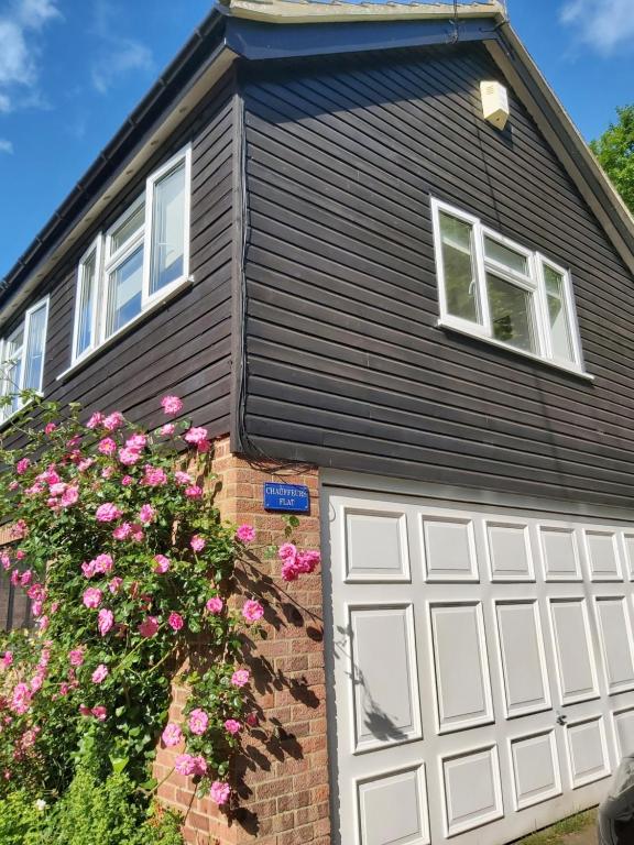 una casa con una puerta de garaje blanca y flores rosas en Chauffeur's, Snape, en Saxmundham