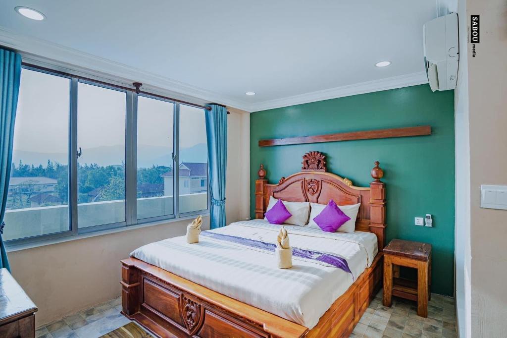 a bedroom with a bed with green walls and windows at Neakru Guesthouse and Restaurant in Kampot