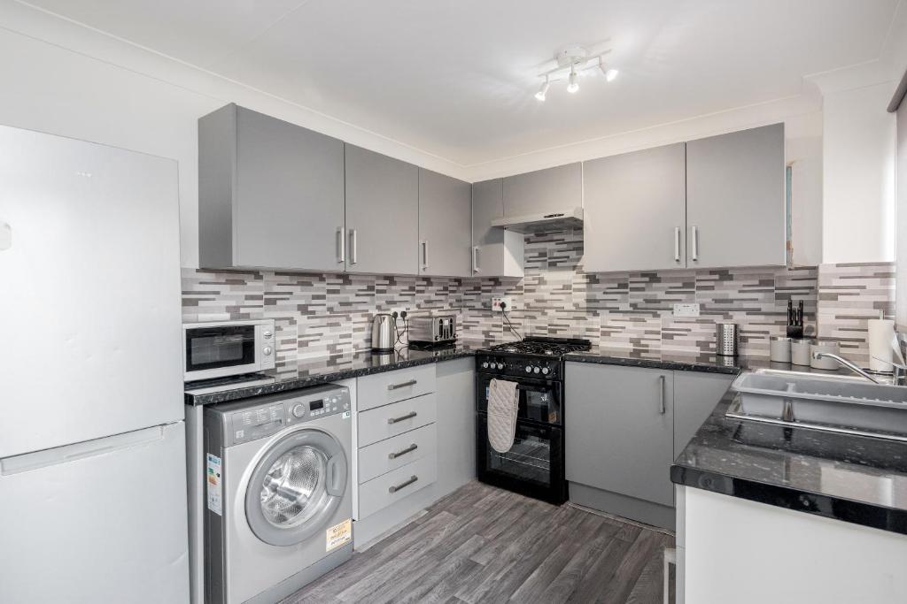 a kitchen with white cabinets and a washer and dryer at Tms Lovely 3 Bed House-Tilbury-Free parking in Tilbury