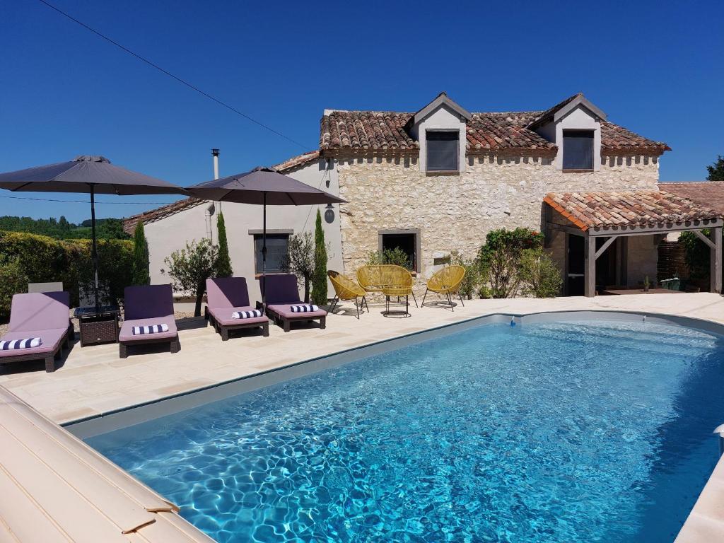 a pool with chairs and umbrellas in front of a house at Maison Vigneronne in Villeneuve-de-Duras
