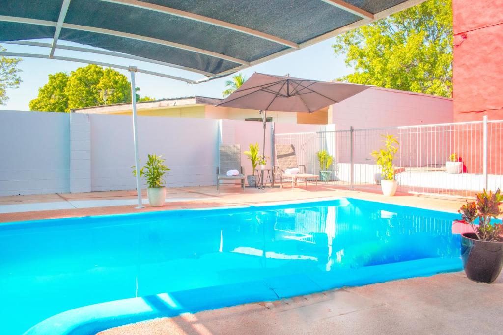 a blue swimming pool with an umbrella and a house at K - Town Hotel in Katherine