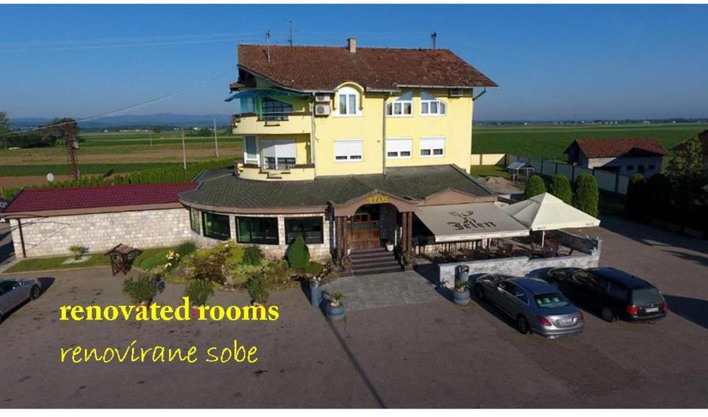 a large yellow house with two cars parked in a parking lot at Motel Atos in Laktaši