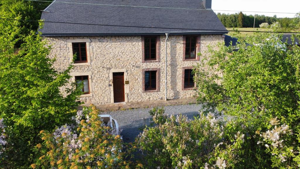 una casa de piedra con techo negro y árboles en L'Antre Parenthèse de Sainte-Cécile en Florenville