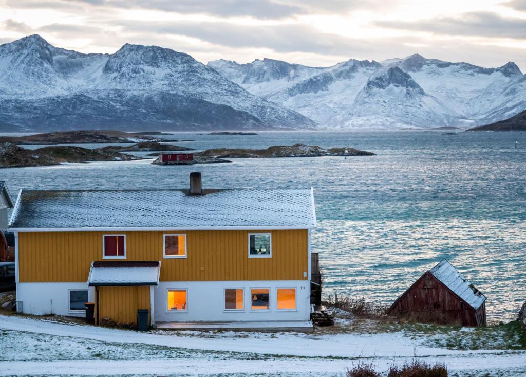 una casa en la nieve con montañas en el fondo en Cozy apartment by the sea, en Tromsø