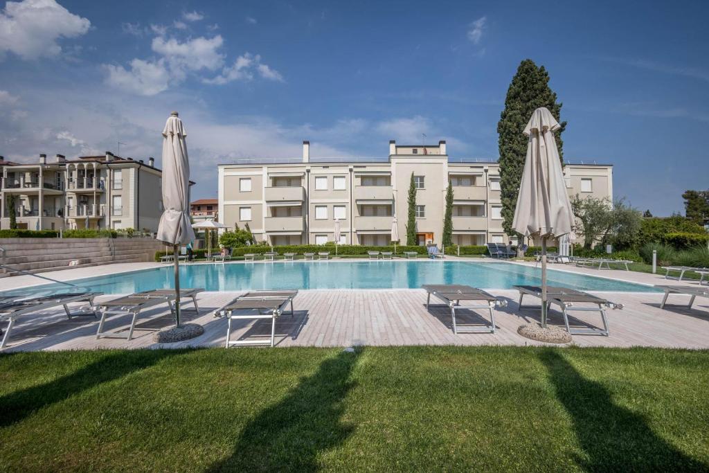 a swimming pool with umbrellas and chairs and a building at Appartamento Madeleine in Toscolano Maderno