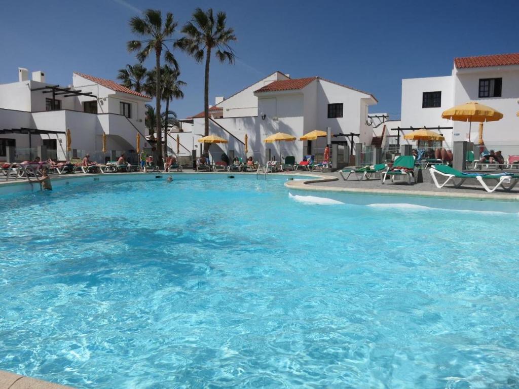 a large swimming pool with blue water in a resort at Lovely newly refurbished 1 Bedroom Flat Minutes From Sandy Beach,private terrace in Caleta De Fuste