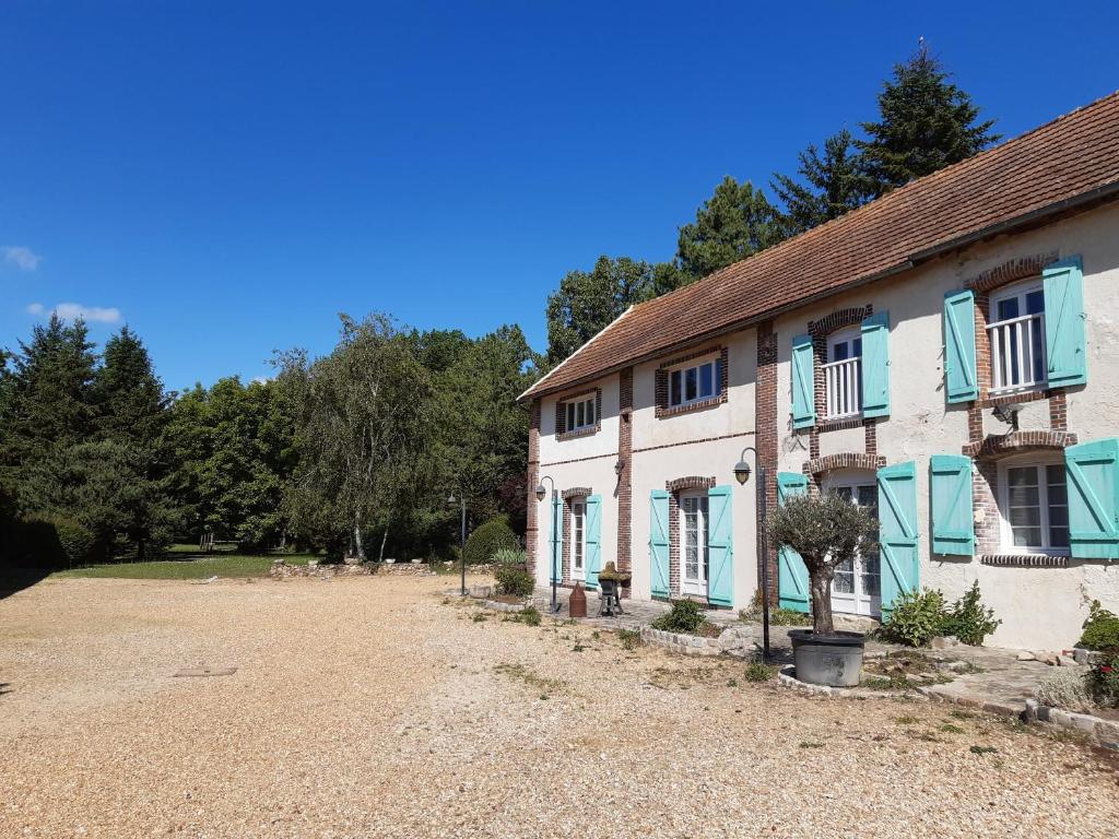 une maison avec des fenêtres bleues et une allée en gravier dans l'établissement Au Charme de l'Eure, à Villiers-le-Morhier