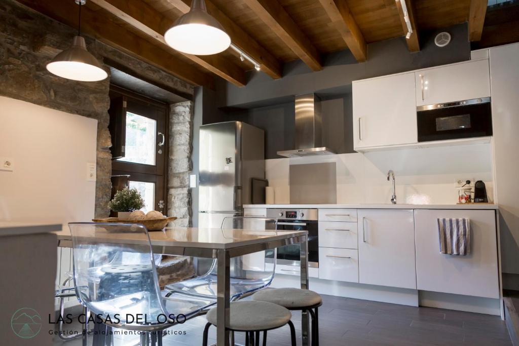 una cocina con armarios blancos, mesa y taburetes en El Torreón - Las Casas del Oso en Proaza