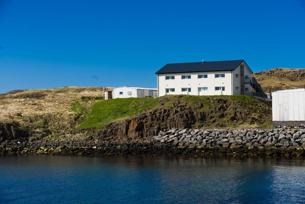 a white house on top of a hill next to the water at Salthús Guesthouse in Skagaströnd