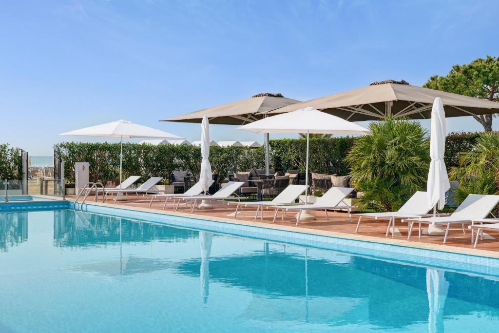 a swimming pool with lounge chairs and umbrellas at Hotel Delle Rose in Lido di Jesolo