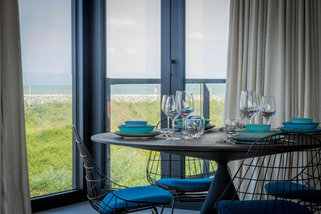 a table with chairs and wine glasses in front of a window at Rots in de Branding Luxurious 2 bedroom apartment in the dunes with sea sight in Cadzand