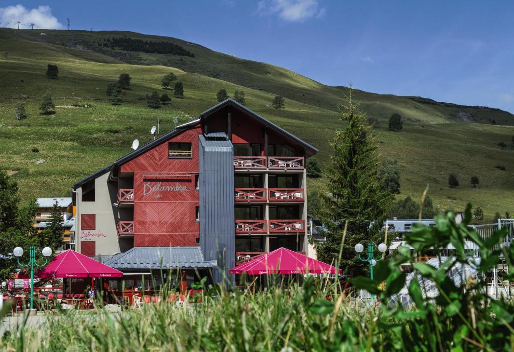 a red building with red umbrellas next to a hill at Hôtel Les 2 Alpes L'Orée Des Pistes in Les Deux Alpes