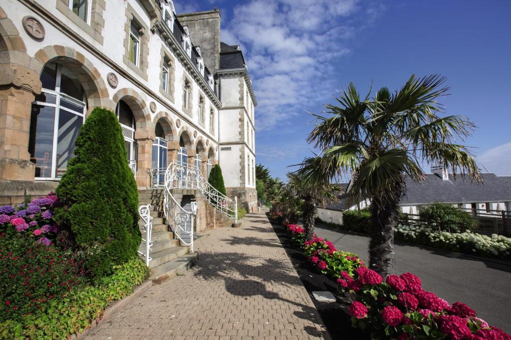 un edificio con una palmera y flores delante de él en Belambra Clubs Trégastel - Le Castel Sainte Anne en Trégastel