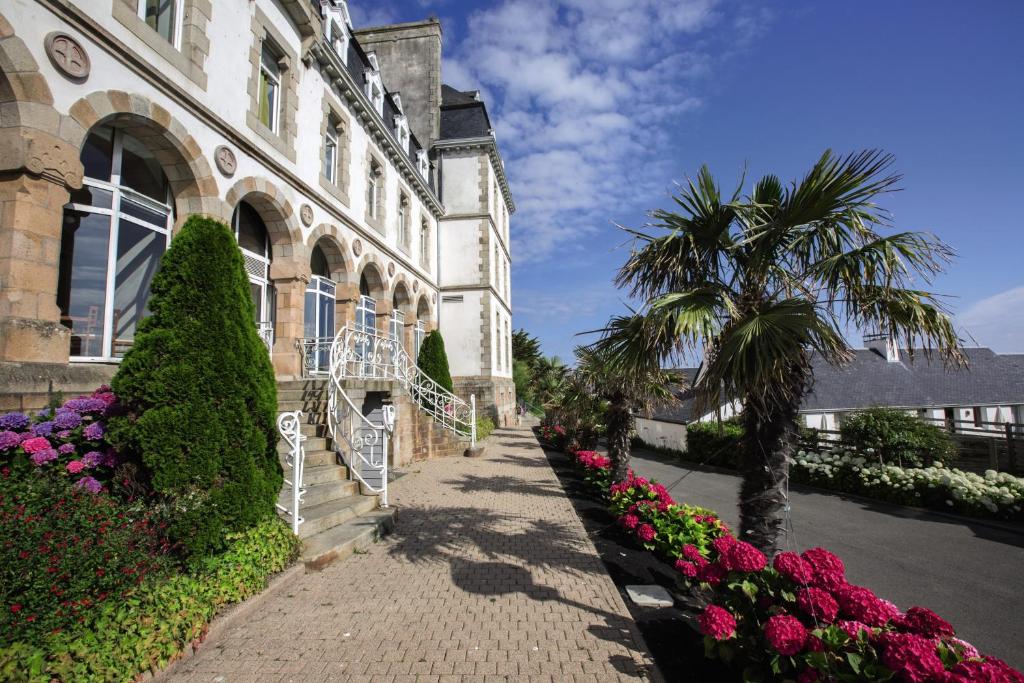un edificio con una palmera y flores delante de él en Belambra Clubs Trégastel - Le Castel Sainte Anne, en Trégastel