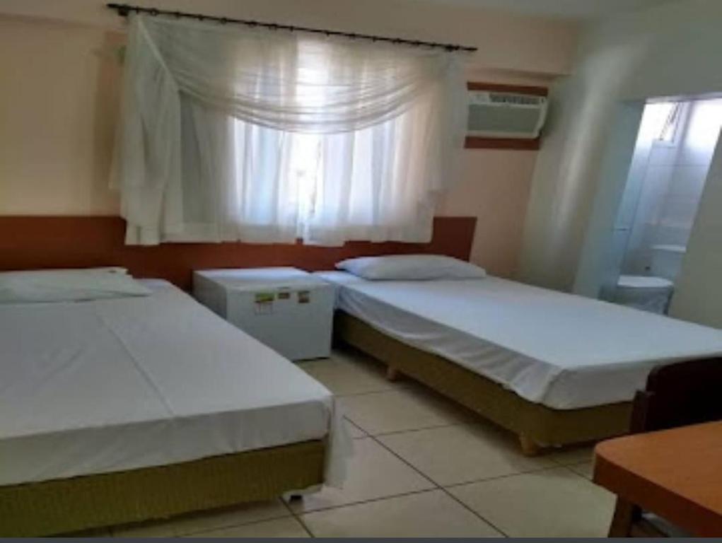 two beds in a small room with a window at Novo Grande Hotel in Ribeirão Preto