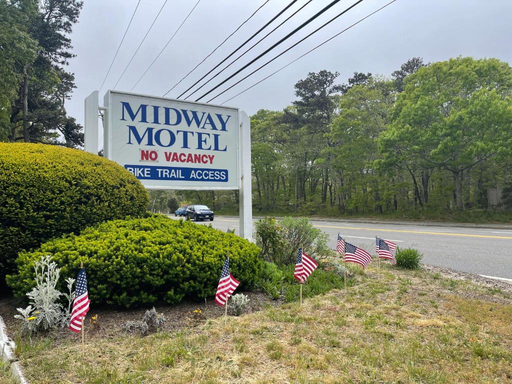 Um sinal para um motel com bandeiras americanas na berma da estrada. em Midway Motel & Cottages em Eastham