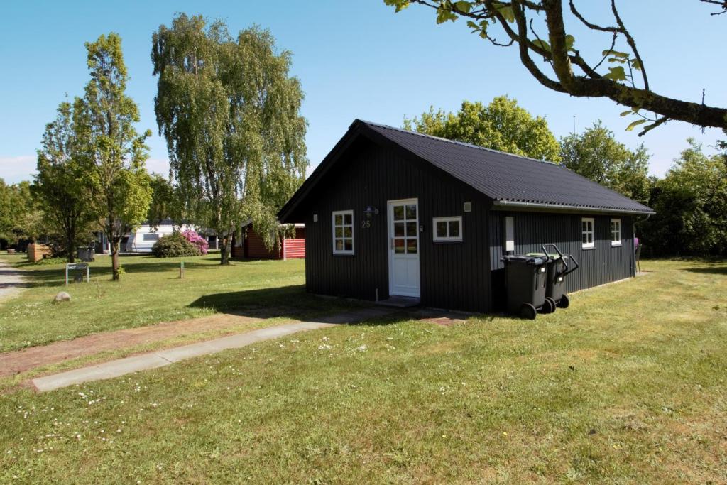 a black building in a yard with a trash can at Hovborg Ferieby - Torpet 25 in Hovborg