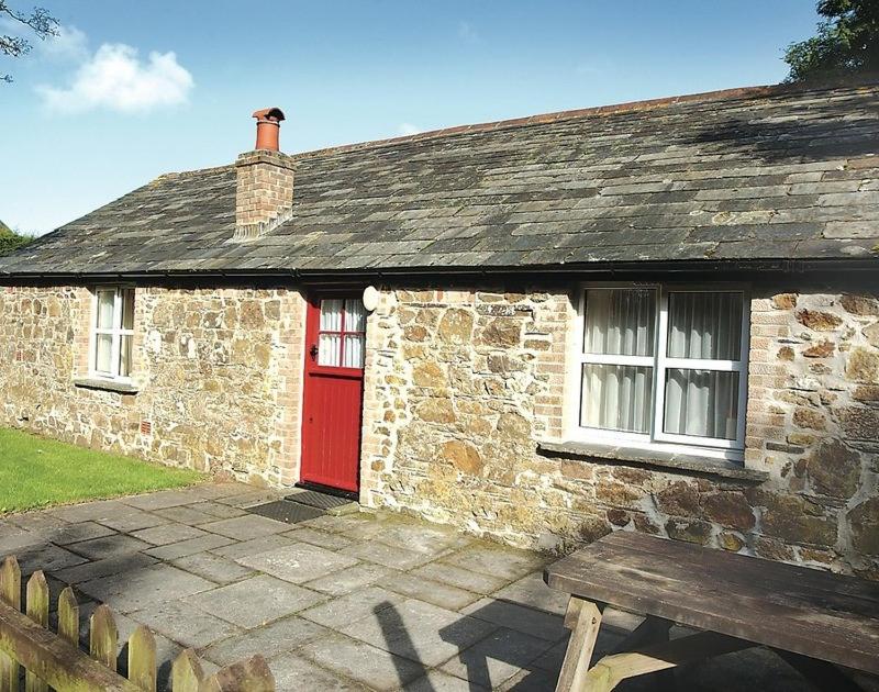 a stone house with a red door and a bench at Mill Pond in Saint Minver