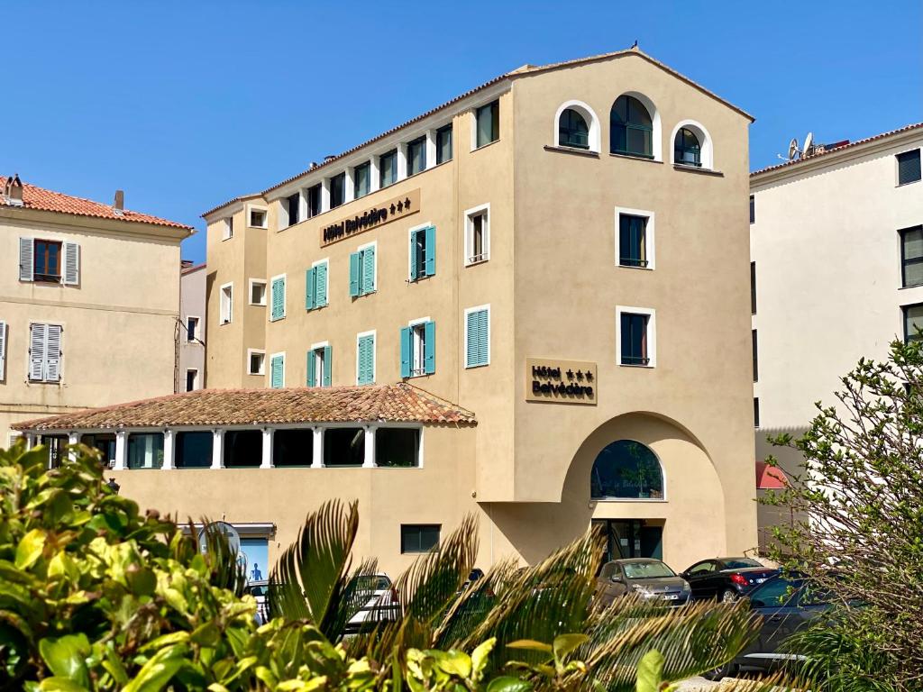 un grand bâtiment avec des voitures garées devant lui dans l'établissement Hotel Belvedere, à Calvi