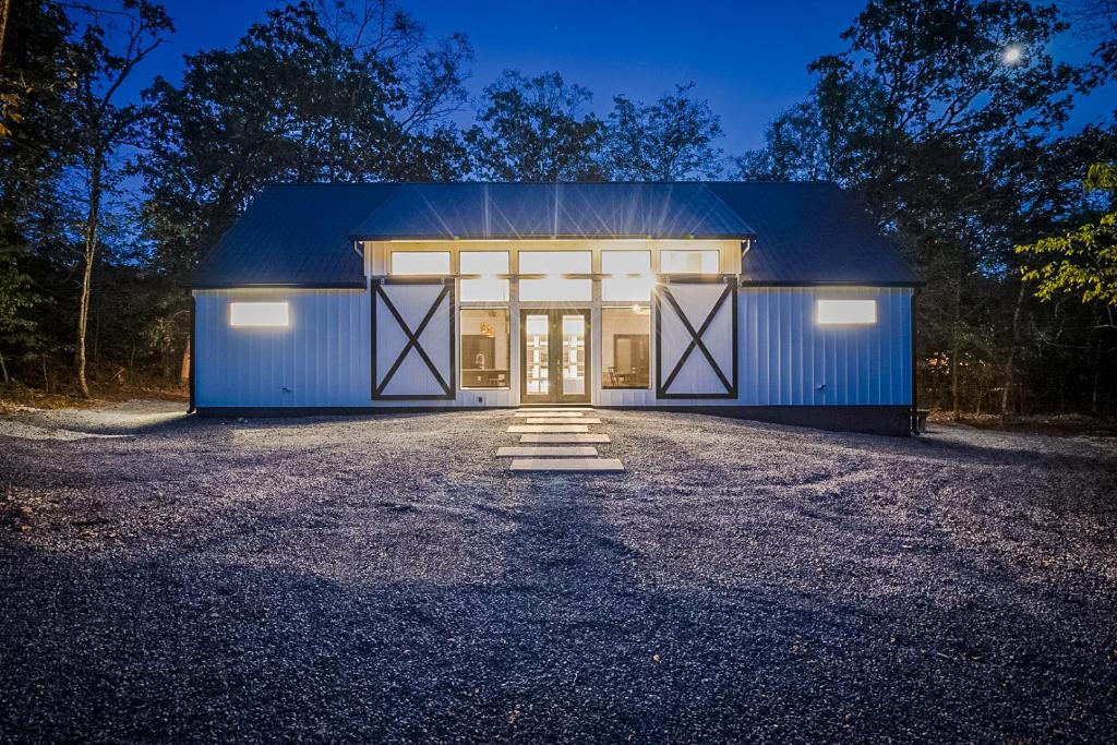 a large blue barn with doors on a driveway at "The Barndo" 4BR Luxury Cabin, Hot Tub, Fire Pit, Bunks, Arcades, Playhouse! in Broken Bow