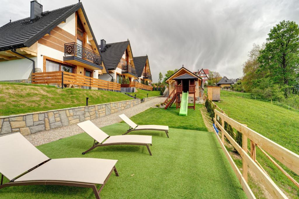a house with a yard with chairs and a playground at Komfortowe domki na wynajem - Holiday Tatry in Poronin