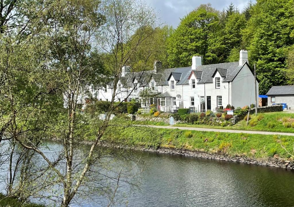 a large white house next to a river at Coorie Doon in Cairnbaan