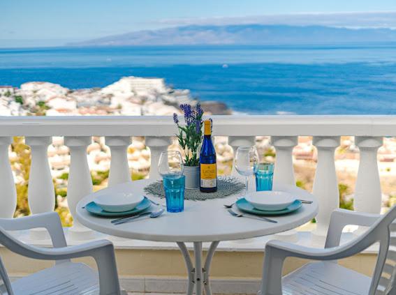 una mesa con 2 sillas y una botella de vino en el balcón en Cosy Seaview Apartment, en Santiago del Teide