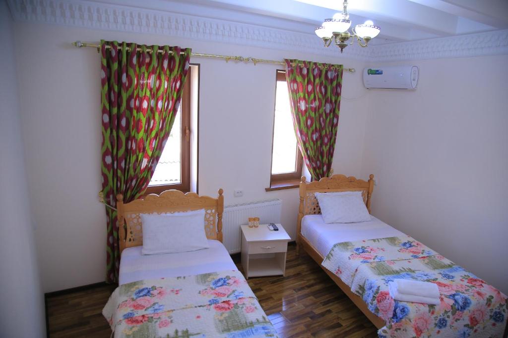 two beds in a room with two windows at Hotel Mironshox in Bukhara