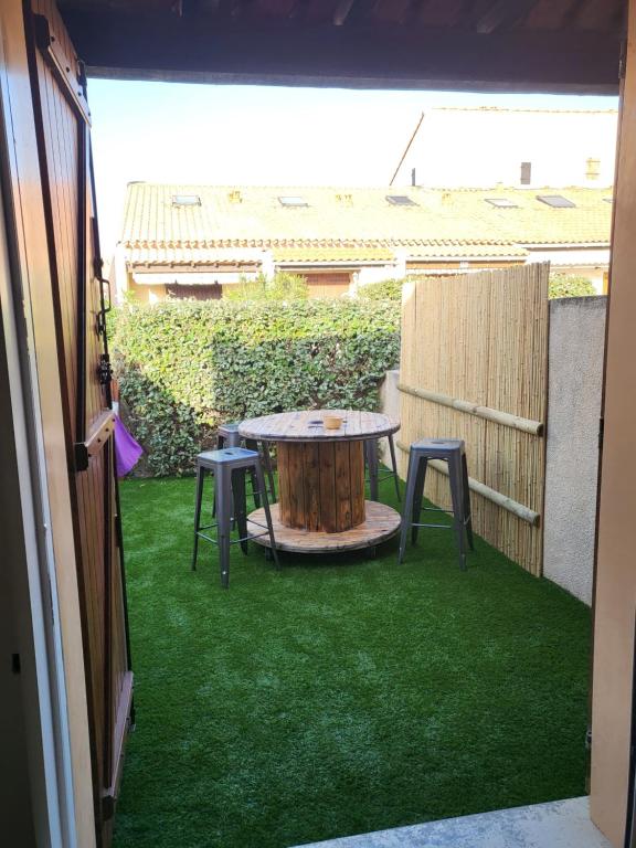 eine Terrasse mit einem Tisch und zwei Hockern auf dem Rasen in der Unterkunft Villa bord de mer avec belle terrasse in Port Leucate