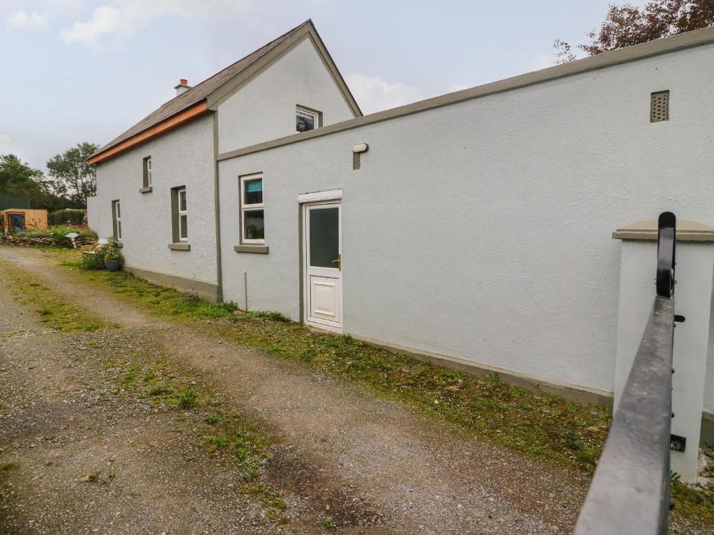 a white building with a door next to a dirt road at Lehane's Cottage in Macroom