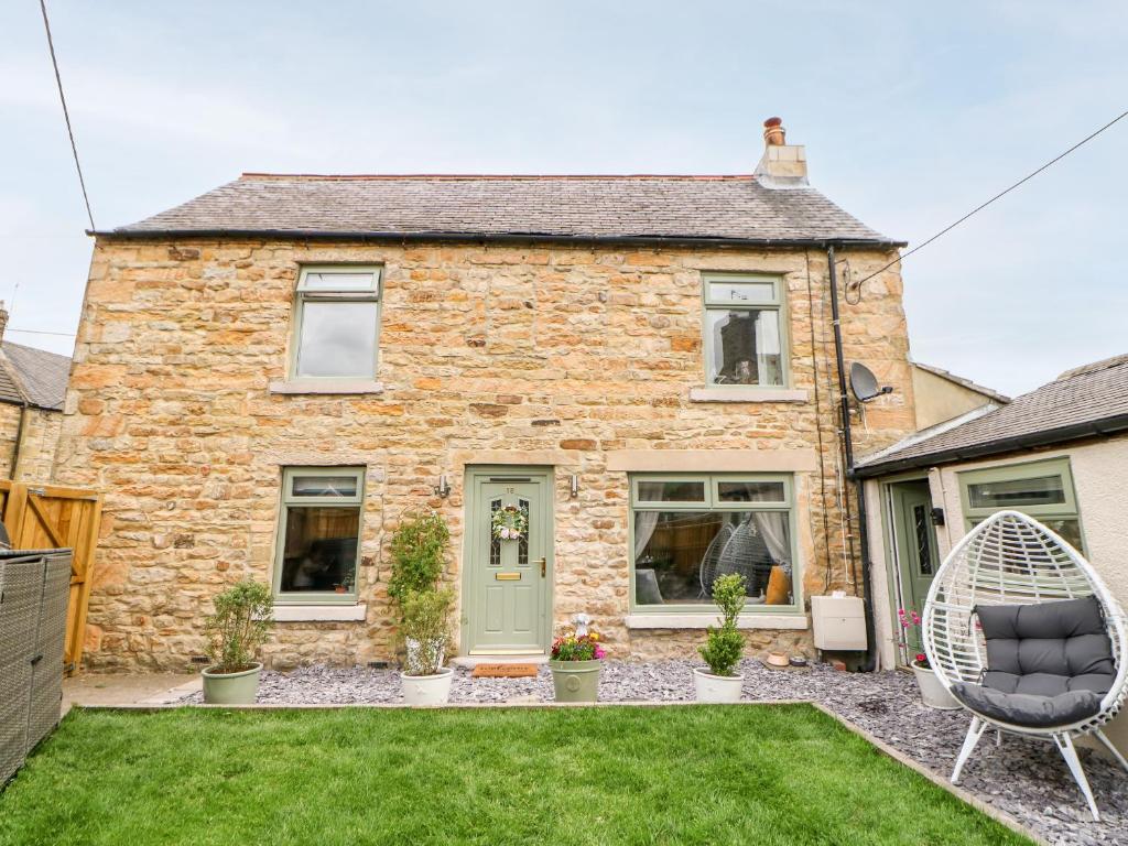 an old stone house with a chair in the yard at Pepper Cottage in Bishop Auckland