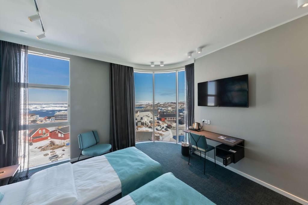 a hotel room with a bed and a desk and a large window at Best Western Plus Hotel Ilulissat in Ilulissat