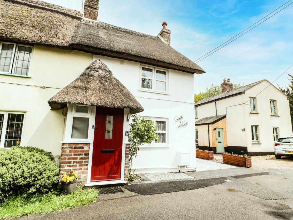 a thatch roof house with a red door at Cosynook Cottage in Blandford Forum