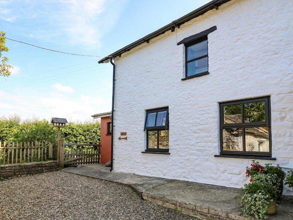 a white cottage with black windows and a fence at Barley Cottage in Mydroilin