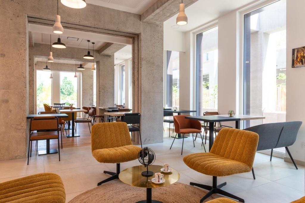 un restaurante con mesas, sillas y ventanas en The Originals Résidence Le Monde Paris Ivry Confluence en Ivry-sur-Seine