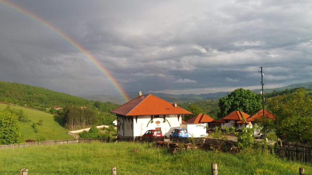 um arco-íris sobre uma casa com carros num campo em Etno selo Lelić em Valjevo