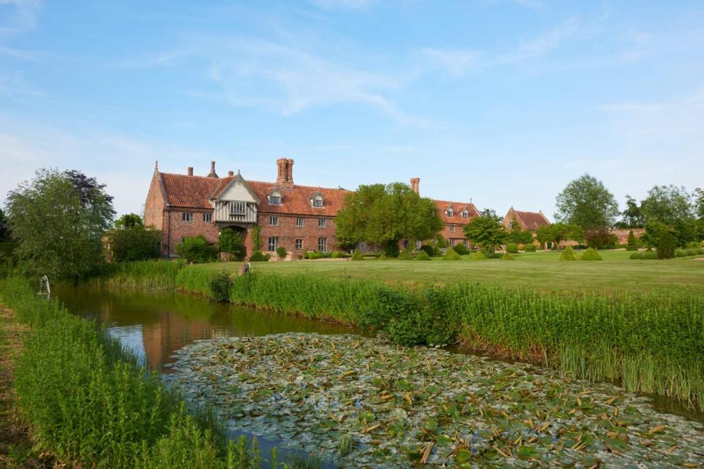 une maison et une rivière devant un bâtiment dans l'établissement A Luxury Tudor Hall & Gardens Located on Breath-Taking Norfolk Estate, à Norwich