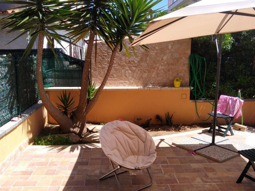 eine Terrasse mit 2 Stühlen, einem Sonnenschirm und Palmen in der Unterkunft Casa a 50 passi dalla spiaggia in Capoterra