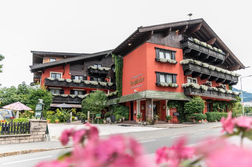 Un bâtiment rouge avec des fleurs devant lui dans l'établissement Hotel Bruggwirt, à St. Johann in Tirol