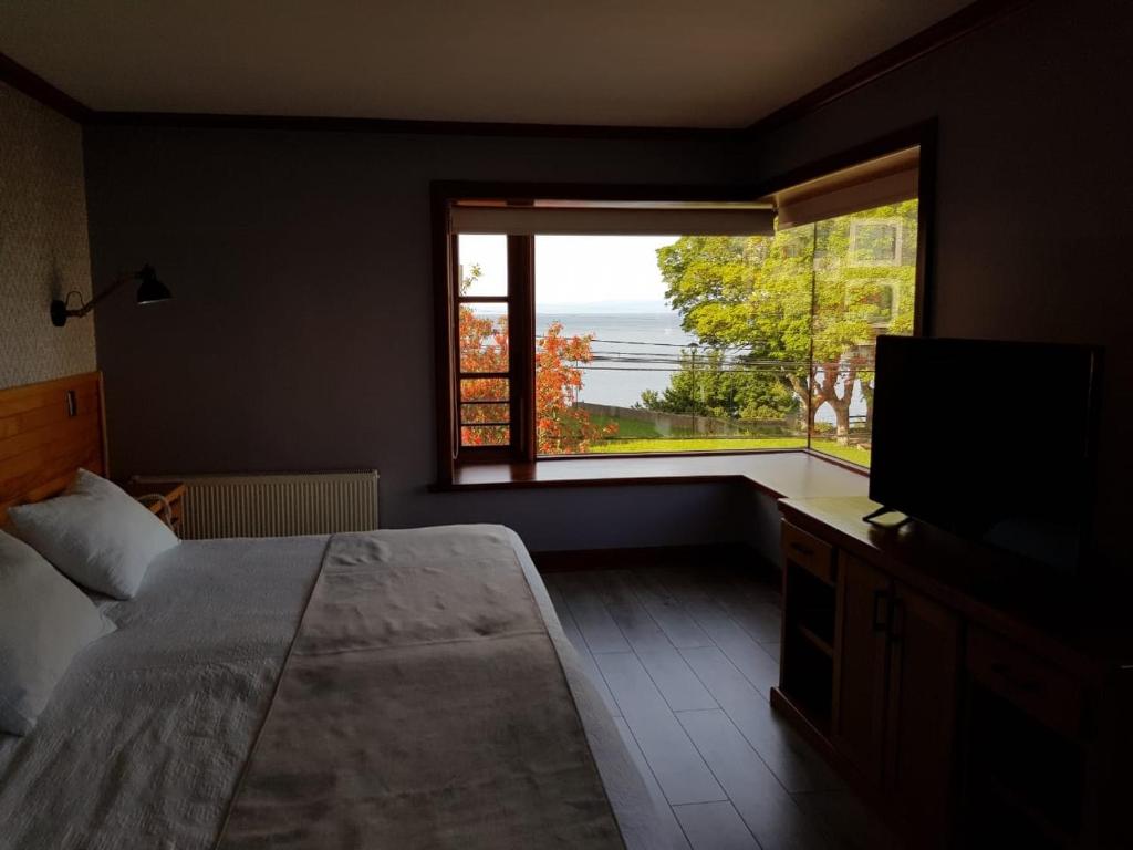 1 dormitorio con 1 cama, TV y ventana en Hotel Puelche, en Puerto Varas